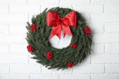 Beautiful Christmas wreath with red berries and bow hanging white brick wall