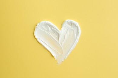 Photo of Samples of face cream in shape of heart on yellow background, top view