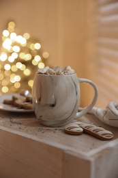 Photo of Tasty hot drink and cookies against Christmas lights