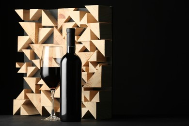 Photo of Stylish presentation of red wine in bottle and wineglass on table against black background, space for text