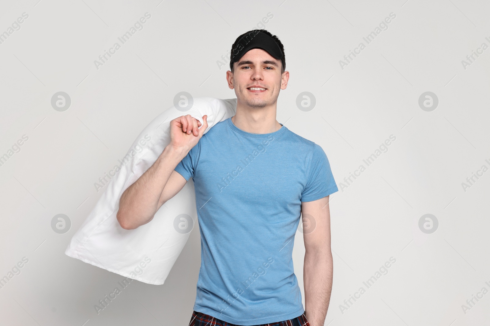 Photo of Happy man in pyjama and sleep mask holding pillow on light grey background