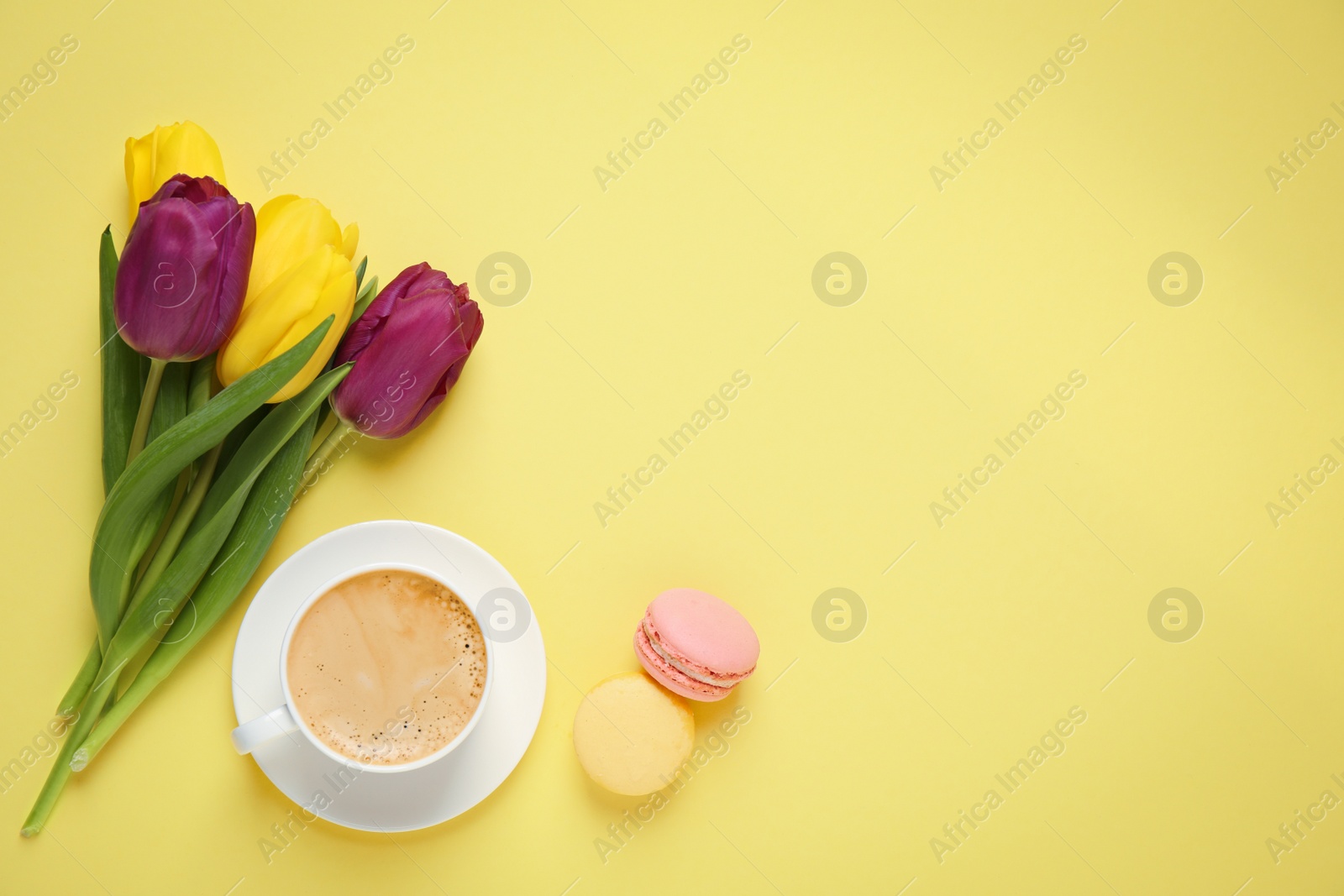 Photo of Delicious morning coffee, macarons and flowers on yellow background, flat lay. Space for text