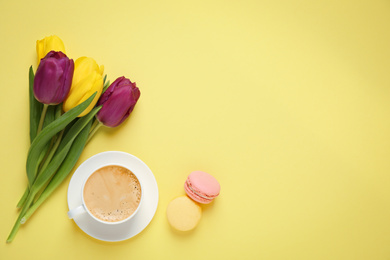 Photo of Delicious morning coffee, macarons and flowers on yellow background, flat lay. Space for text