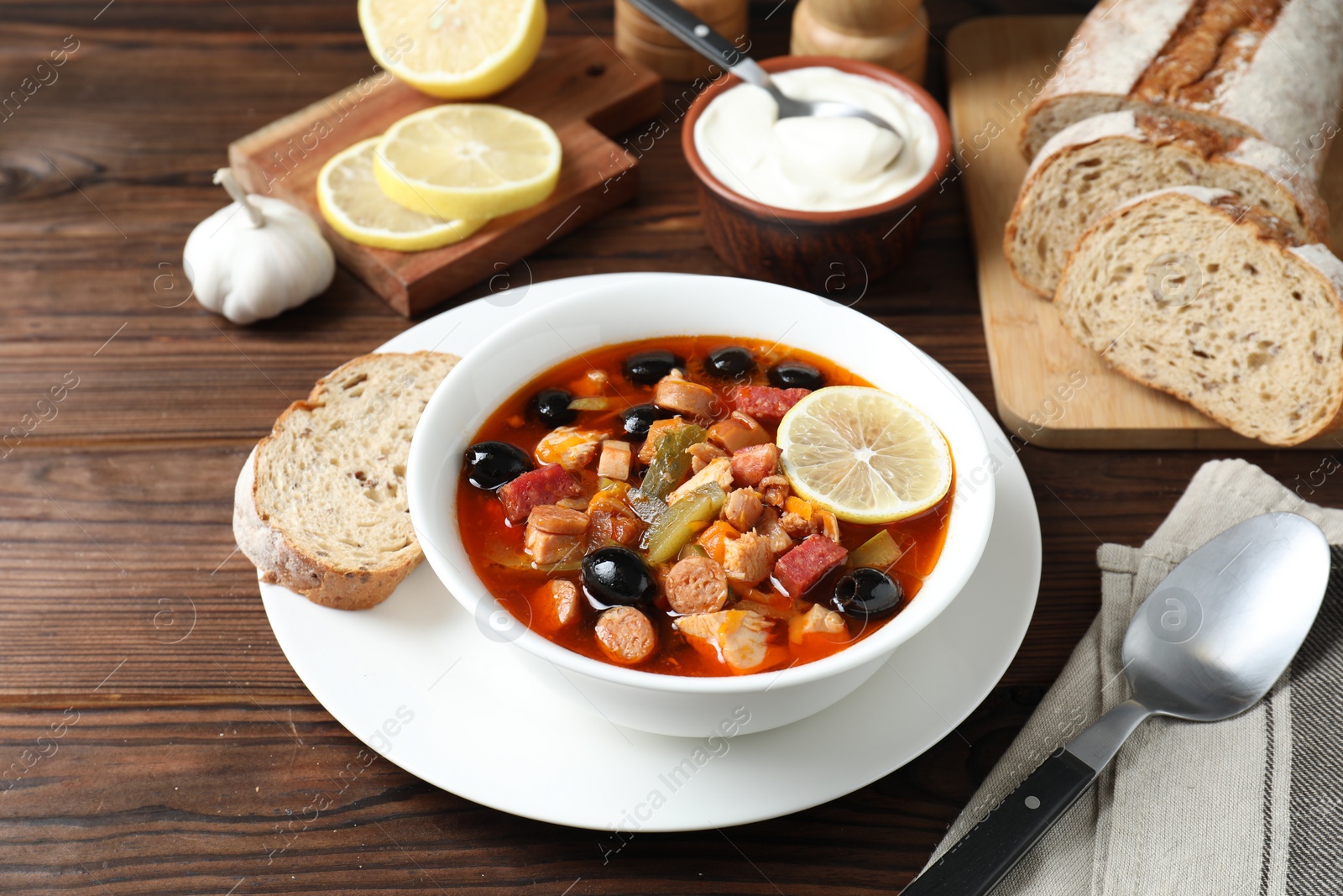 Photo of Meat solyanka soup with sausages, olives and vegetables served on wooden table