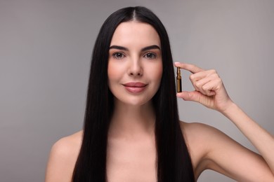 Beautiful young woman holding skincare ampoule on grey background