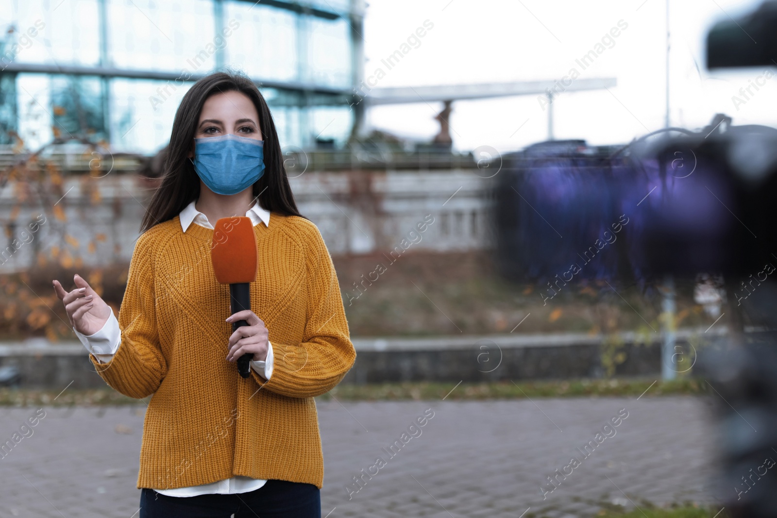 Image of Young journalist with medical mask and microphone working on city street. Virus protection