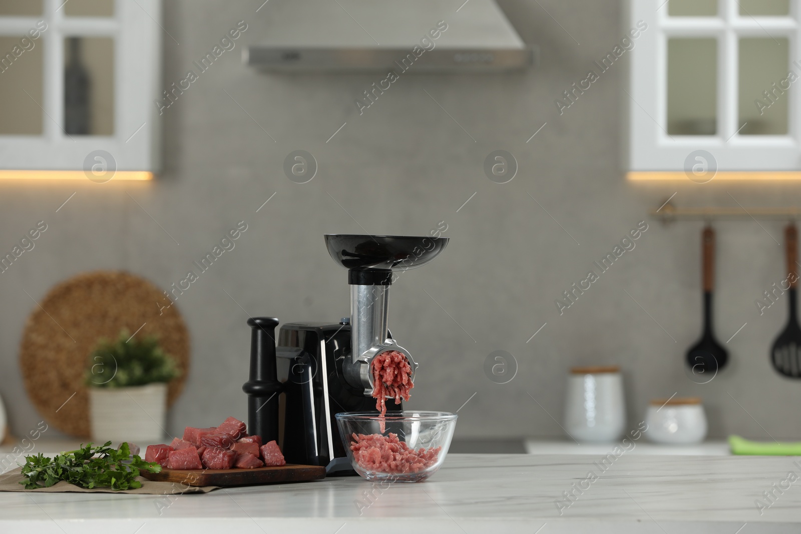 Photo of Electric meat grinder with beef mince and parsley on white table in kitchen, space for text