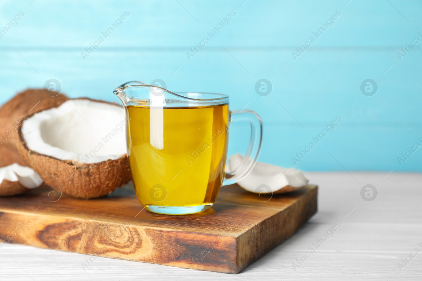 Photo of Ripe coconut and oil in pitcher on wooden table. Healthy cooking