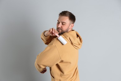 Photo of Young man cleaning clothes with lint roller on grey background