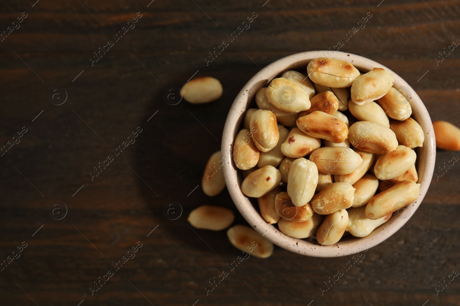 Photo of Roasted peanuts in bowl on wooden table, top view. Space for text