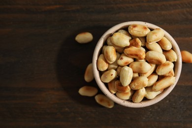 Photo of Roasted peanuts in bowl on wooden table, top view. Space for text