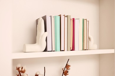 Beautiful hand shaped bookends with books on shelf indoors