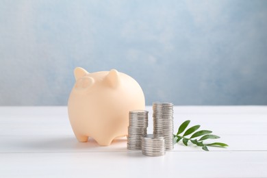 Financial savings. Piggy bank, stacked coins and green twig on white wooden table