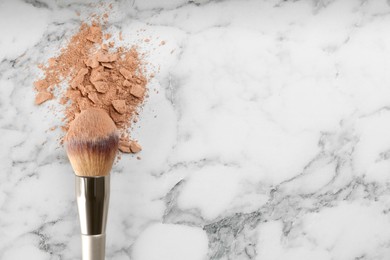 Photo of Makeup brush and scattered face powder on white marble table, top view. Space for text