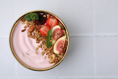 Bowl with yogurt, fruits and granola on white tiled table, top view. Space for text