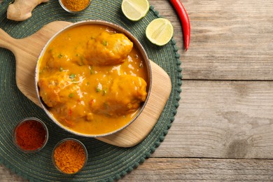 Photo of Tasty chicken curry and ingredients on wooden table, flat lay. Space for text