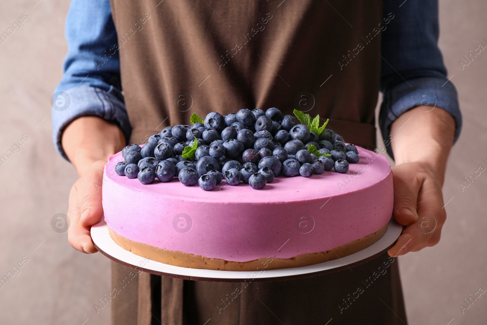 Photo of Young woman holding tasty blueberry cake on beige background, closeup