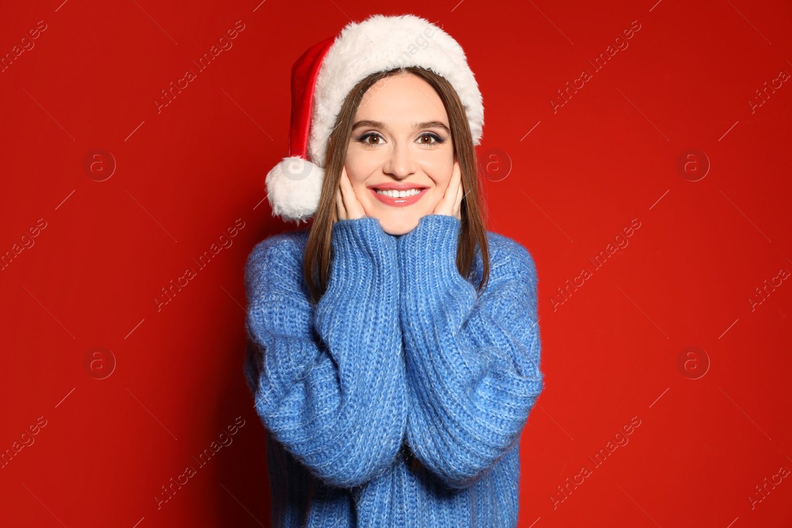 Photo of Young woman in Christmas sweater and Santa hat on red background