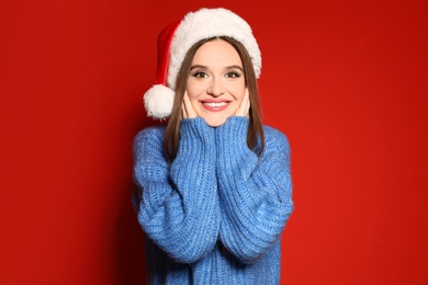 Young woman in Christmas sweater and Santa hat on red background