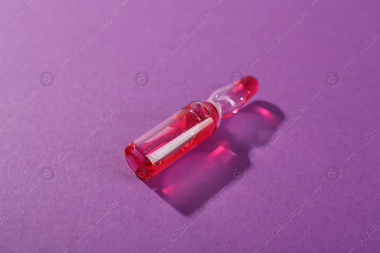 Photo of Glass ampoule with liquid on purple background