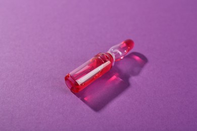 Photo of Glass ampoule with liquid on purple background