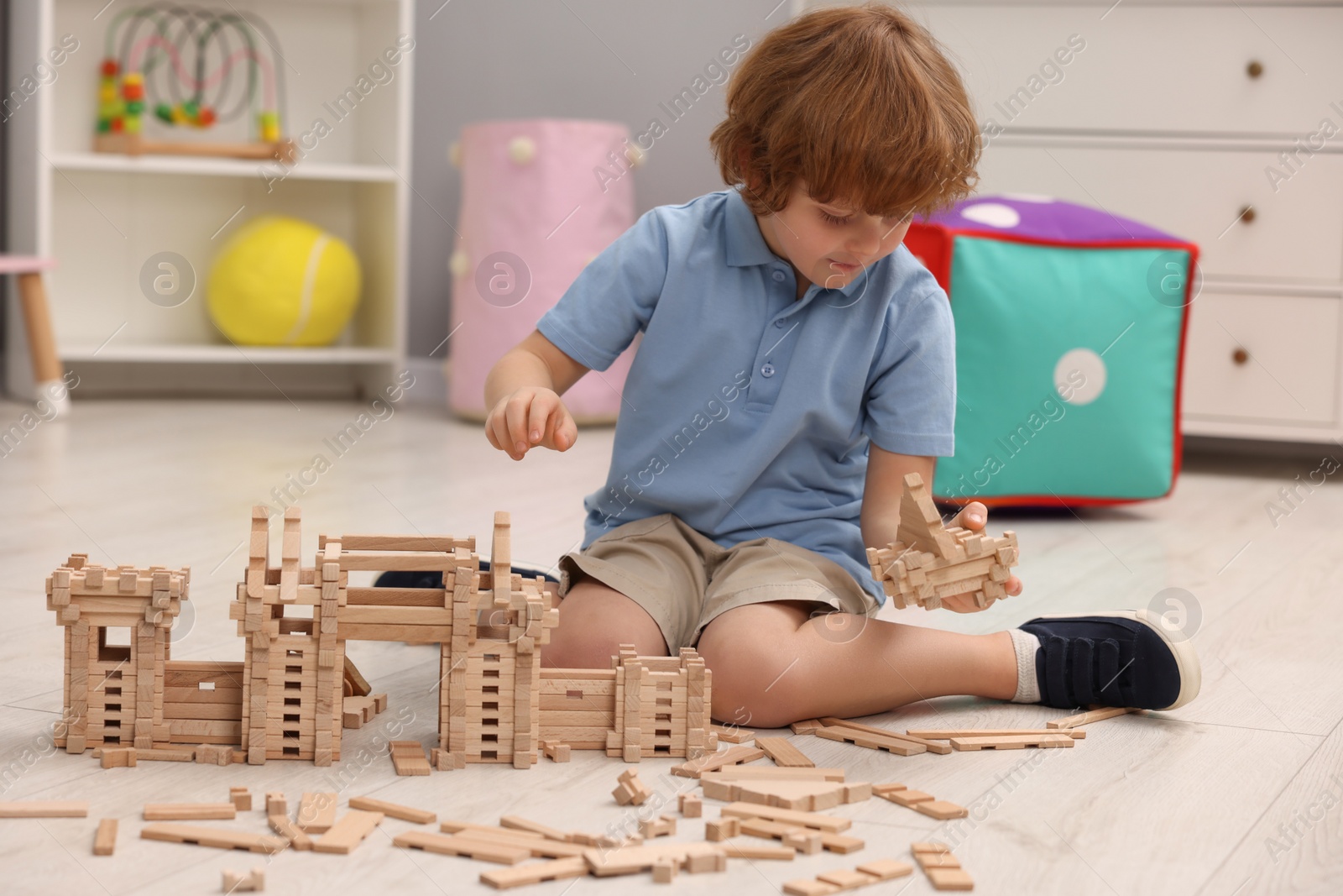 Photo of Little boy playing with wooden construction set on floor in room. Child's toy