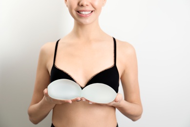 Woman holding silicone implants for breast augmentation on white background, closeup. Cosmetic surgery