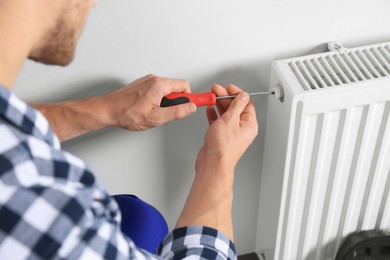 Photo of Professional plumber using screwdriver while preparing heating radiator for winter season, closeup