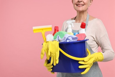 Housewife holding bucket with cleaning supplies on pink background, closeup. Space for text