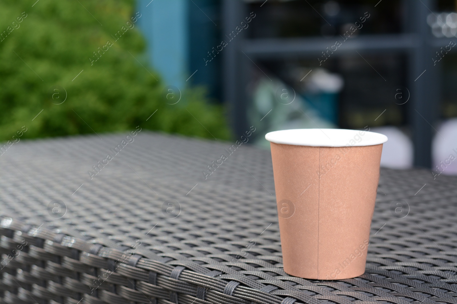 Photo of Coffee cardboard cup on rattan table outdoors, space for text