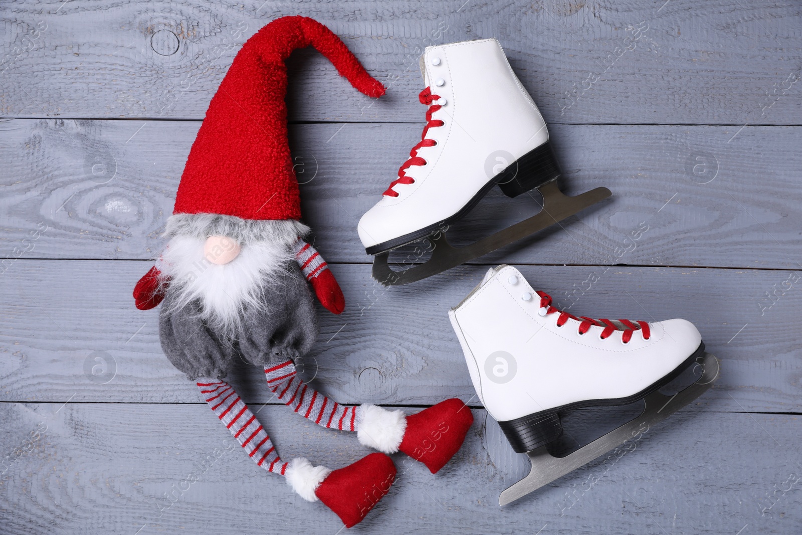 Photo of Pair of ice skates with Christmas gnome on grey wooden background, flat lay