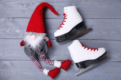 Pair of ice skates with Christmas gnome on grey wooden background, flat lay