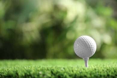 Photo of Golf ball with tee on artificial grass against blurred background, space for text