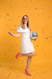 Photo of Happy young woman with disco ball and confetti on yellow background