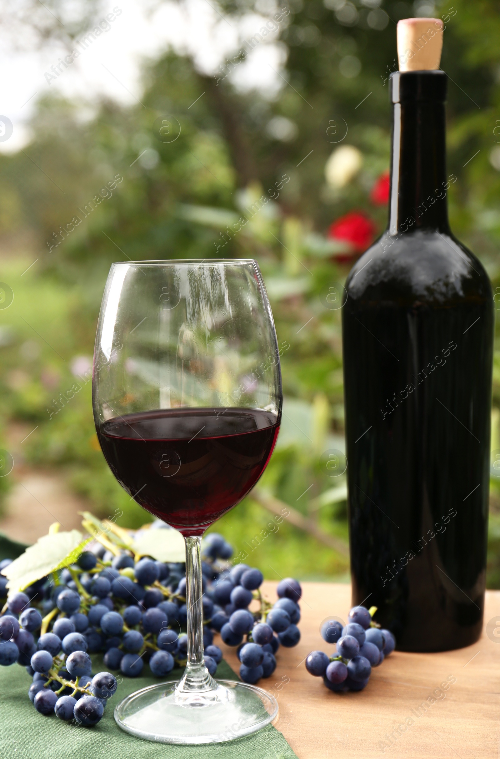 Photo of Red wine and grapes on wooden table outdoors