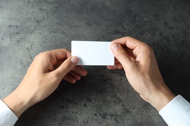 Man holding blank cards at black textured table, top view. Mockup for design