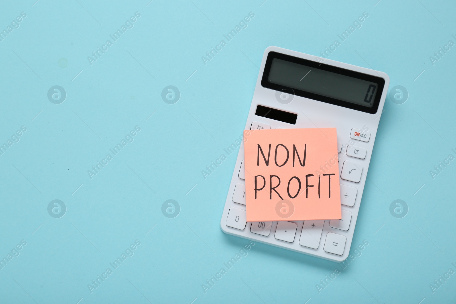 Photo of Paper note with phrase Non Profit and calculator on light blue background, top view. Space for text