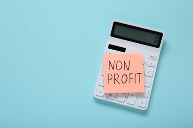 Paper note with phrase Non Profit and calculator on light blue background, top view. Space for text