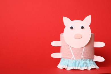Photo of Toy pig made of toilet paper roll on red background. Space for text