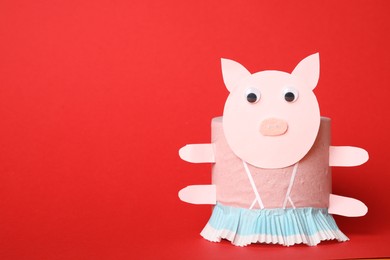 Toy pig made of toilet paper roll on red background. Space for text