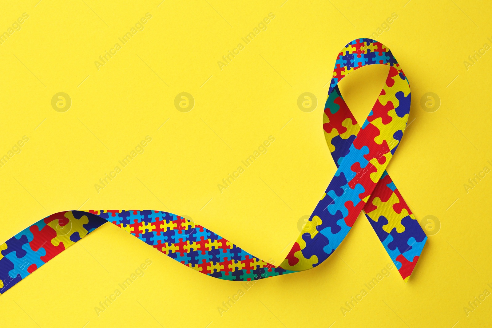 Image of World Autism Awareness Day. Colorful puzzle ribbon on yellow background, top view