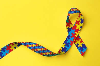 World Autism Awareness Day. Colorful puzzle ribbon on yellow background, top view