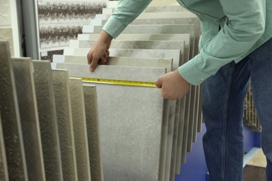 Photo of Man using tape measure while choosing tile in store, closeup