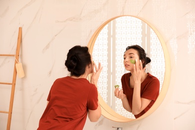 Young woman applying mask on her face near mirror in bathroom