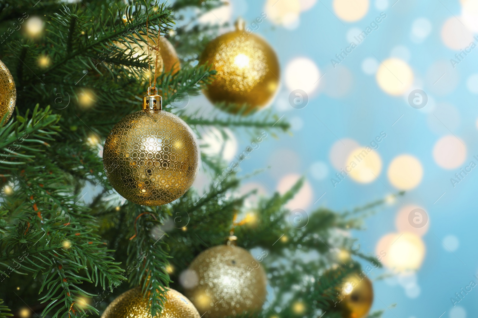 Image of Beautiful Christmas tree with bright baubles against blurred lights on light blue background, closeup. Space for text