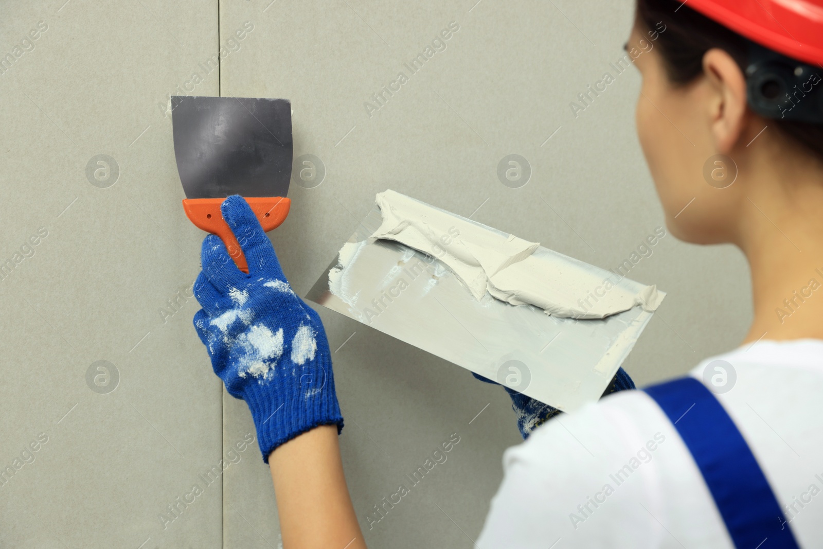 Photo of Professional worker plastering wall with putty knives, closeup