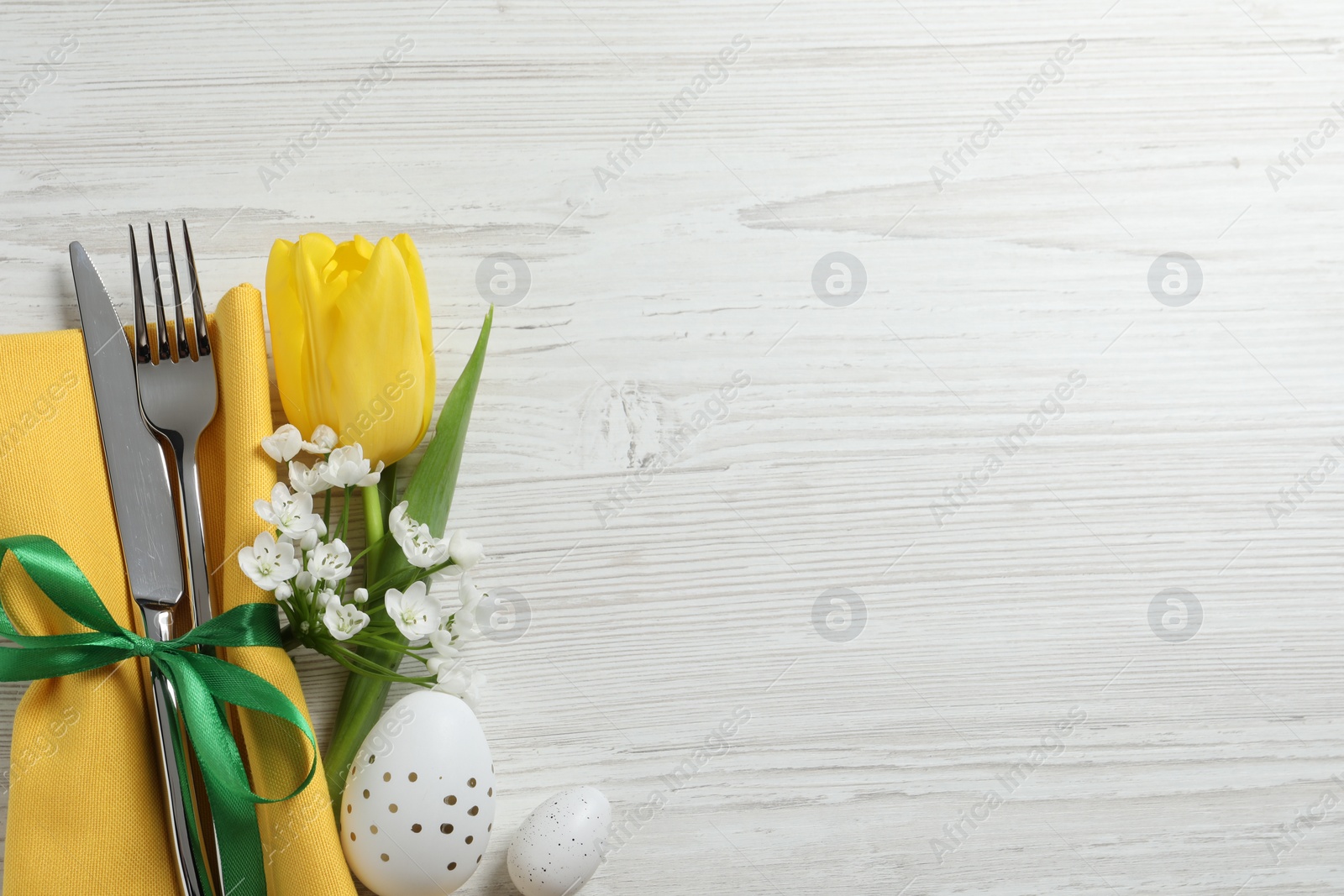 Photo of Cutlery set, Easter eggs and beautiful flowers on white wooden table, flat lay. Space for text