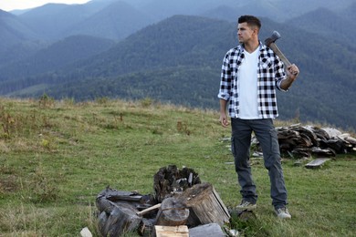 Handsome man with axe and cut firewood in mountains