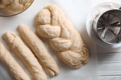 Photo of Homemade braided bread and ingredients on white wooden table, flat lay. Cooking traditional Shabbat challah