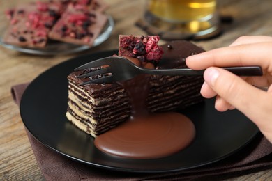Photo of Woman eating tasty chocolate cake at wooden table, closeup